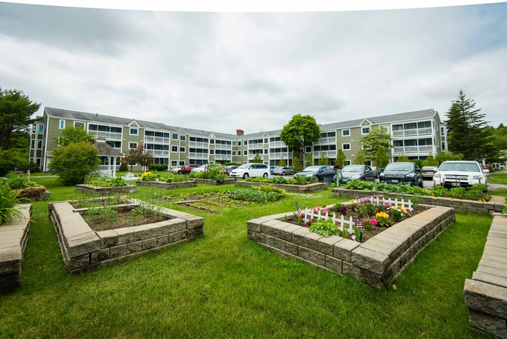 The Highlands senior living community building in the background, and blower garden beds in the foreground at The Highlands, a reliable assisted living option near Brunswick, Maine.